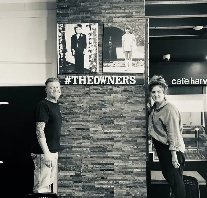 Phil and Laura, the owners of Cafe Harvest, standing beneath their childhood photos inside the cafe